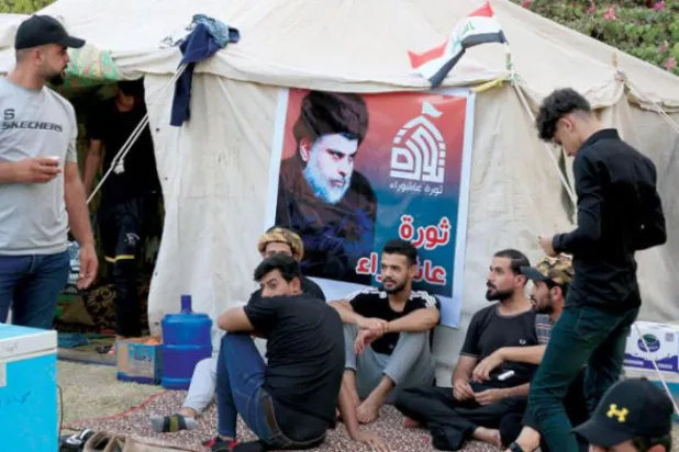بغداد میں عراقی پارلیمنٹ کی عمارت کے سامنے لگائے گئے خیموں کے پاس الصدر کے حامی بیٹھے ہیں۔ (ای.پی. اے)