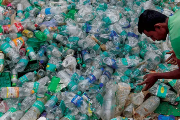 عامل يفرز الزجاجات البلاستيكية في مكب نفايات (أ.ف.ب)