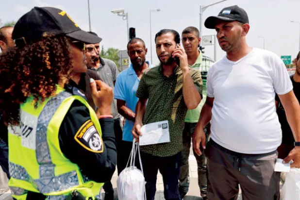 شرطية إسرائيلية تتحدث إلى عمال فلسطينيين لم يتمكنوا من العودة إلى غزة بعدما فرض الإغلاق في 4 أغسطس (رويترز)
