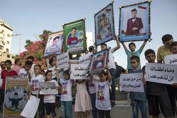 Filistinli çocuklar, İsrail’in Cebaliye'deki Felluce Mezarlığı’na düzenlediği saldırıda hayatını kaybeden çocukların fotoğraflarını elinde tutuyor (AP)
