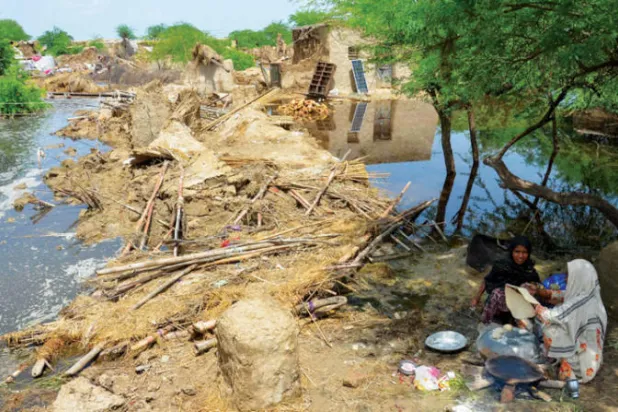 سيدتان تعجنان وتخبزان عند ما تبقى من قريتهما التي غمرتها الفيضانات ودمرتها في منطقة جعفر آباد (أ.ف.ب)