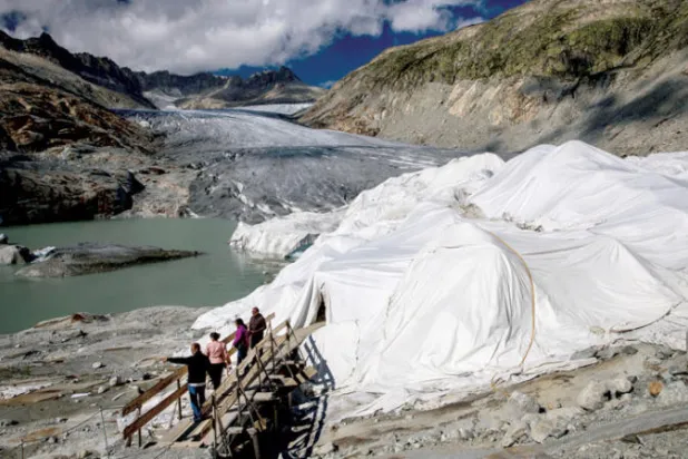 مجموعة من السياح امام كهف ثلجي مغطى بمواد لحمايته من الذوبان في اوبرغومز في سويسرا (رويترز)