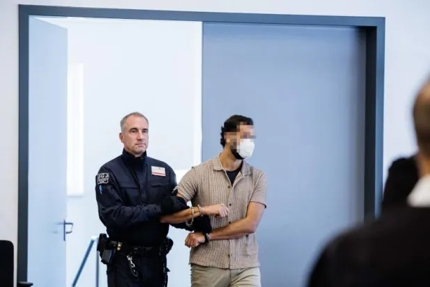 شرطي يمسك بأحد المتهمين أثناء وصوله إلى قاعة محكمة دريسدن بشرق ألمانيا (أ.ف.ب)