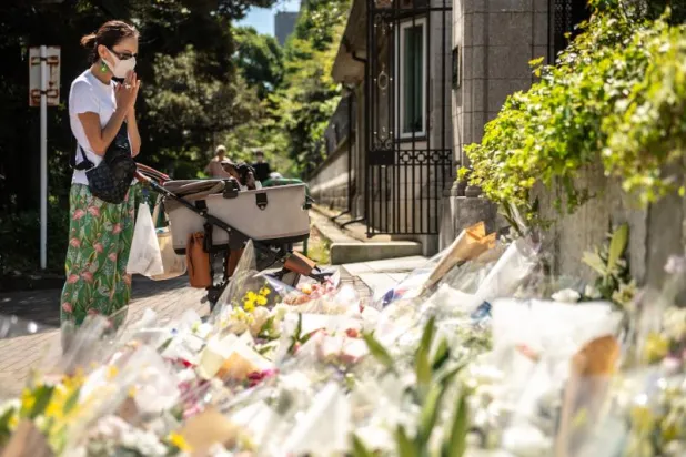 سيدة تقف أمام زهور موضوعة أمام السفارة البريطانية في طوكيو تعزية للملكة البريطانية إليزابيث الثانية (أ.ف.ب)