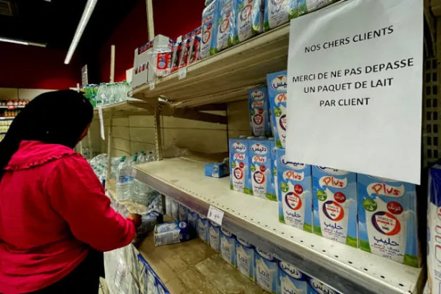 تونسية تتبضع في أحد المتاجر بينما اللافتة بالفرنسية تحظر شراء أكثر من عبوة لبن واحدة لكل مشتر (رويترز)