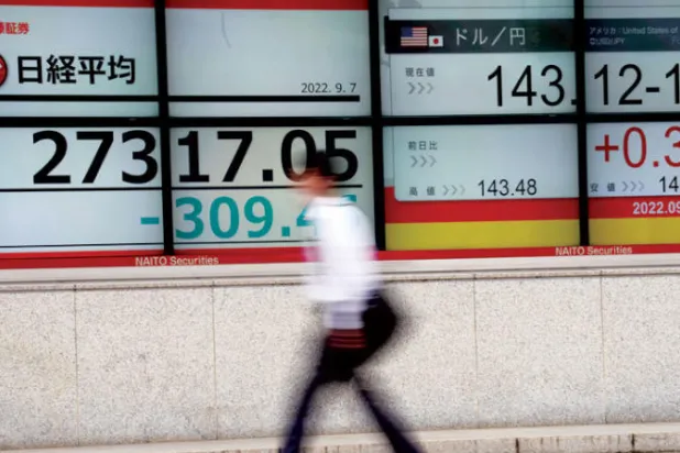 شخص يمشي أمام لوحة أسهم إلكترونية تعرض مؤشر نيكاي 225 الياباني وسعر صرف الدولار الأميركي / الين الياباني في شركة أوراق مالية في طوكيو (أ.ب)