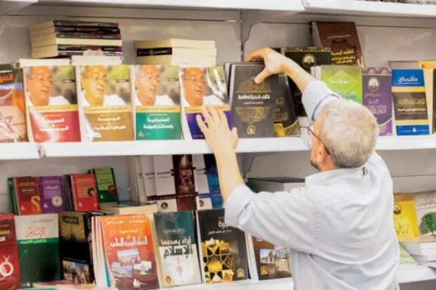 Riyad Kitap Fuarı'ndaki standın raflarını düzenleyen görevli (Yezid Al-Samrani)