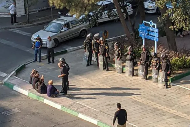 نساء إيرانيات يجلسن بدون حجاب مقابل قوات الأمن في ميدان بطهران (أ.ف.ب)