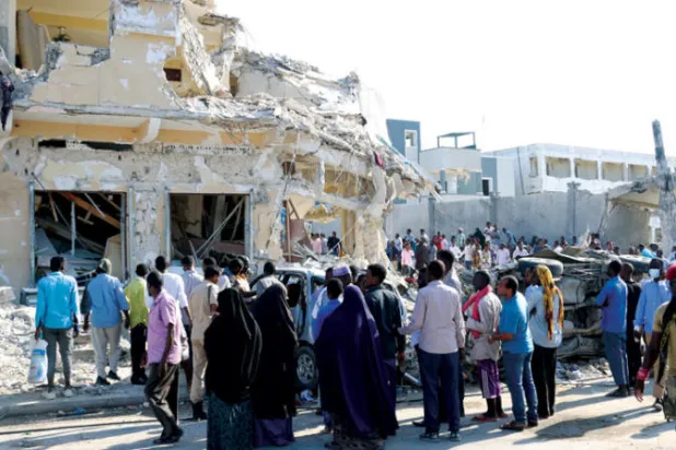 صوماليون يشاهدون مبنى مدمراً في أعقاب تفجيرين في العاصمة مقديشو حيث قُتل ما لا يقل عن 100 شخص وأصيب أكثر من 300 السبت (إ.ب.أ)