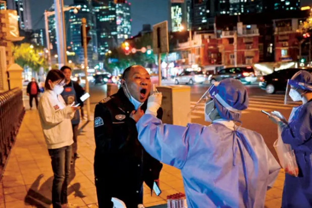 عاملون صحيون يفحصون مواطناً صينياً في شنغهاي بينما تؤثر القيود بشدة على القطاعات الاقتصادية (أ.ف.ب)