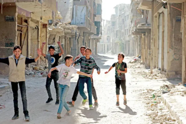 أطفال يلعبون بين أبنية متضررة في مخيم اليرموك الفلسطيني بضواحي دمشق الجنوبية أمس (أ.ف.ب)