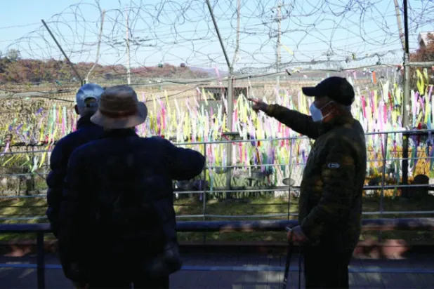أشخاص يقفون عند السياج الحدودي في المنطقة المنزوعة السلاح بين الكوريتين الجمعة (رويترز)