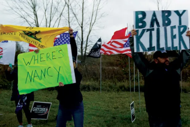 أشخاص يرفعون لافتات تحمل عبارتي «أين هي نانسي» و«قاتل الرضع» في انتظار مرور موكب الرئيس بايدن بإلينوي السبت (رويترز)