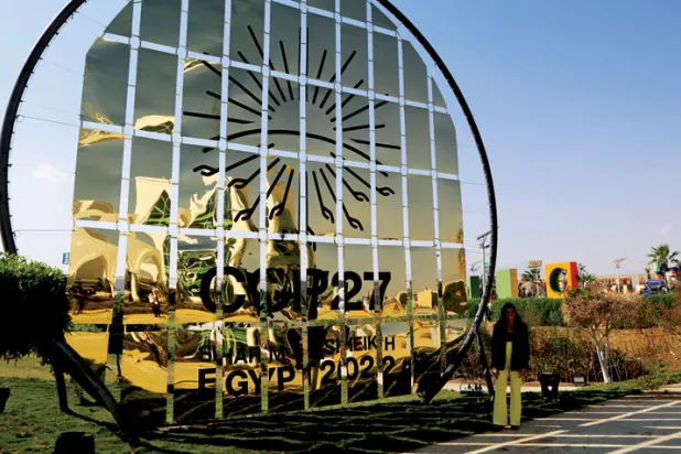 امرأة تقف أمام شعار «كوب27» في شرم الشيخ أمس (أ.ب)