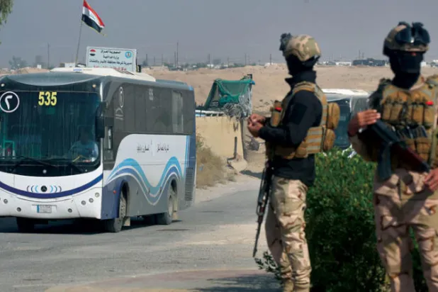جنود عراقيون يحرسون حافلة تقل عوائل نازحة في مخيم للنازحين بالحبانية في محافظة الأنبار (أ.ف.ب)
