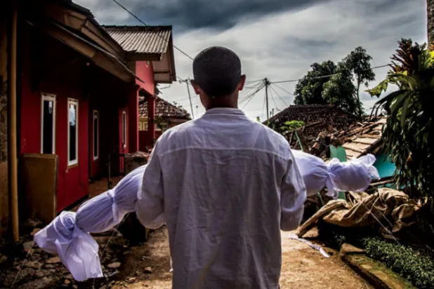 أب يحمل جثة ابنه ملفوفة في كفن أبيض وهو يسير في قريته التي ضربها الزلزال (أ.ف.ب)