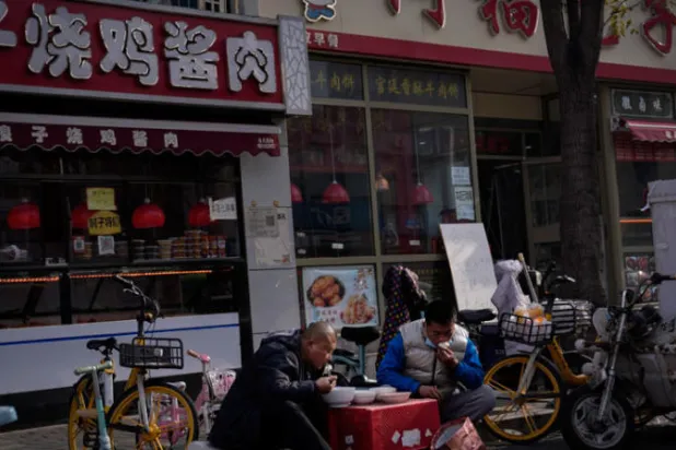 شخصان يتناولان غداءهما خارج مطعم مغلق أمام الزبائن كجزء من سياسة "صفر كوفيد" في بكين التي تضغط على الاقتصاد الصيني (أ.ب)