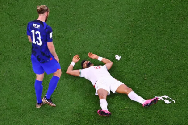 لاعب المنتخب الإيراني رامين رضائيان ممدداً على أرضية ملعب الثمامة بعد إقصاء الولايات المتحدة لبلاده من كأس العالم (رويترز)