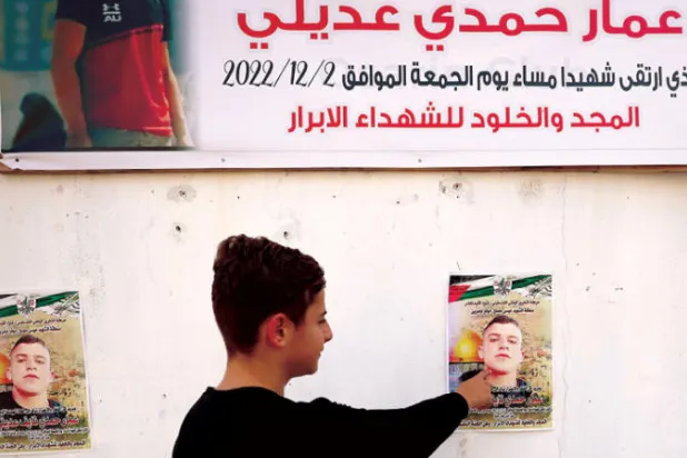 فتى فلسطيني يضع أصبعه على ملصق لعمار مفلح الذي قتله ضابط إسرائيلي الجمعة الفائت (أ.ف.ب)
