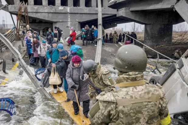 نازحون أوكرانيون يمرون تحت جسر مدمر أثناء فرارهم من القصف الروسي على مدينة أربين شمال غربي كييف (أ.ف.ب)