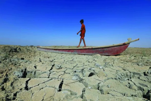 فتى يمشي فوق قارب في قاع هور الجبايش اليابس في جنوب العراق كدليل على التحديات المناخية التي تواجهها البلاد (أ.ف.ب)