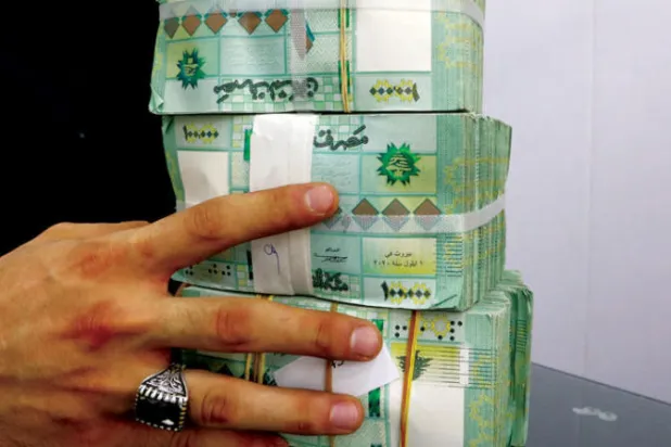 عامل صرافة يحمل رزماً من العملة اللبنانية في أحد محال الصرافة ببيروت (رويترز)