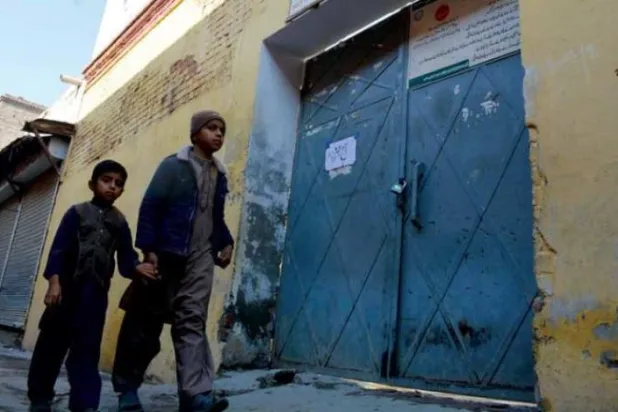 Taliban militanlarının Bannu’daki polis merkezini ele geçirmesinin ardından kapalı bir okulun kapısının önünden geçen çocuklar. Bölgedeki yetkililer kaçırma eylemlerinin yaşanmasından endişe ederek okulları kapatma talimatı verdi. (AFP)