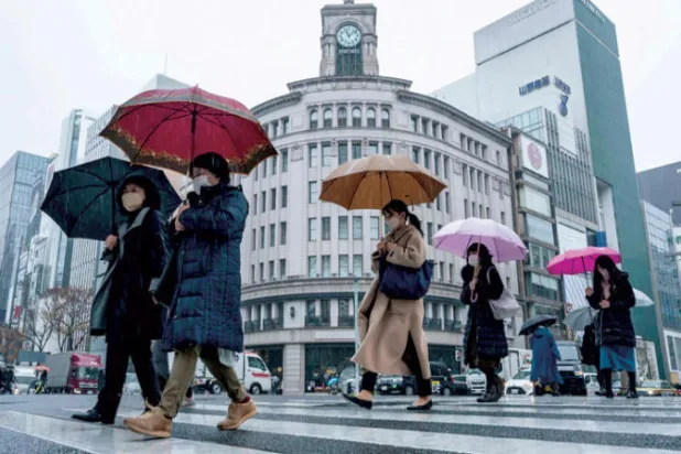 مشاة يعبرون شارعاً وسط الأمطار في العاصمة اليابانية طوكيو (أ.ف.ب)