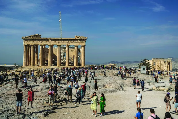 السياح يزورون تلة الأكروبوليس حيث يوجد معبدا البارثينون (يسار) البالغ من العمر 2500 عام وإريخثيون القديم (يمين) في أثينا أكتوبر الماضي (أ.ب)
