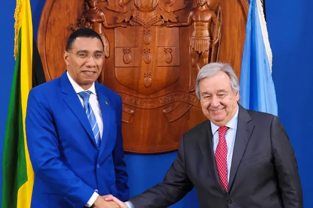 رئيس وزراء جامايكا أندرو هولنس والأمين العام للأمم المتحدة أنطونيو غوتيريش يقفان لالتقاط صورة بينما يتصافحان (رويترز)