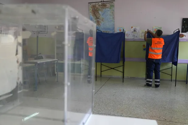 موظف يقوم بتجهيز إحدى غرف الاقتراع في أثينا تحضيراً للانتخابات اليونانية (أ.ب)