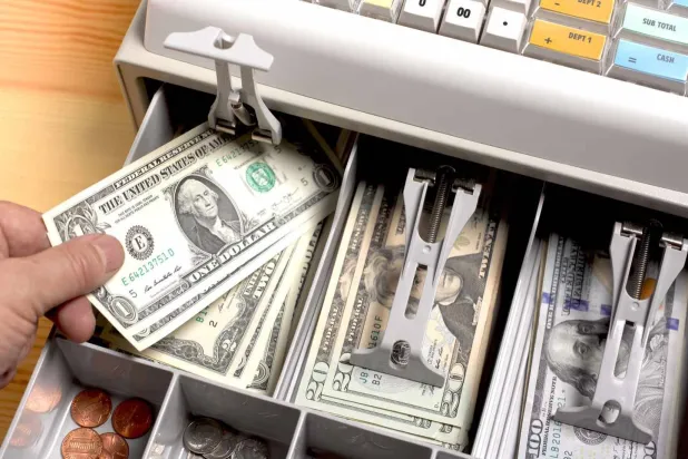 شخص يسحب دولاراً من ماكينة الكاشير في أحد المحال الأميركية (غيتي)