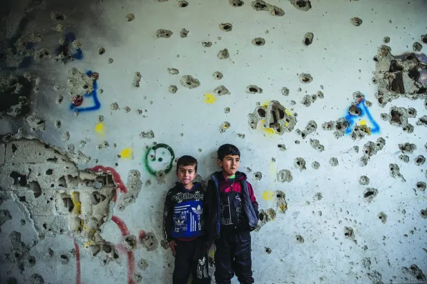 طفلان سوريان يقفان أمس أمام جدار مدرسة شوهته شظايا الرصاص  (د.ب.أ)