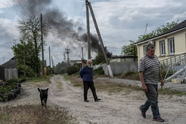 رجلان يسيران وسط ارتفاع أعمدة الدخان بسبب القصف في خاركيف (رويترز)