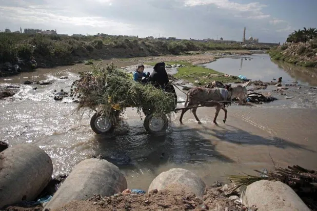 أشخاص يَعبرون فوق مياه صرف صحي بمحيط مدينة غزة في 13 أبريل 2016 (أ.ب)