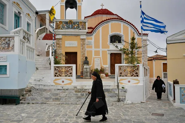 سيدة تسير بجوار كنيسة في قرية أوليمبوس بجزيرة كارباثوس (أ.ف.ب)