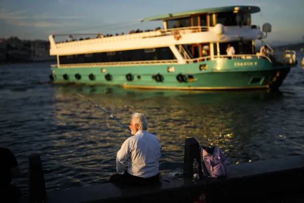 رجل يصطاد السمك عند مرسى العبارات في مضيق البوسفور بمدينة إسطنبول التركية (أ.ب)