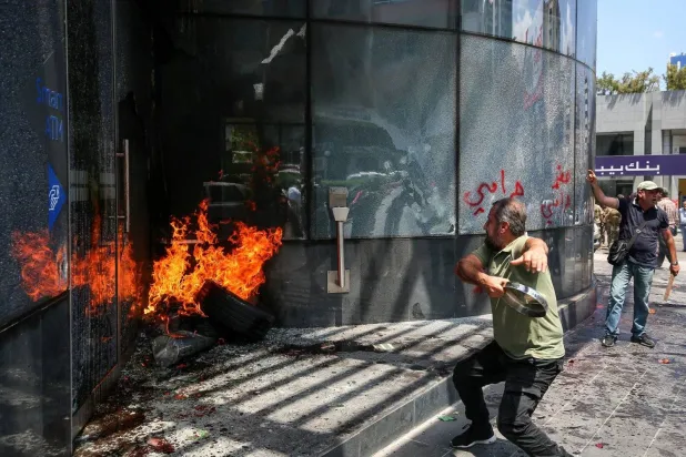 15 June 2023, Lebanon, Beirut: A Lebanese depositor hurls a metal piece at a local bank's facade in the Sin el-Fil suburb east of Beirut. Dozens of Lebanese protesters on Thursday attacked major banks in the nation's capital amid anger over a deepening economic crisis. Photo: Marwan Naamani/dpa