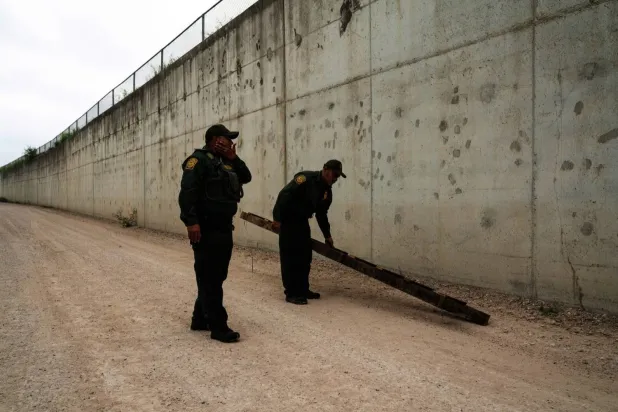 حارسا حدود أميركيان يعاينان سلماً خلَّفه مهاجرون وراءهم عند معبر هيدالغو بالمكسيك في 4 مايو الحالي (أ.ب)