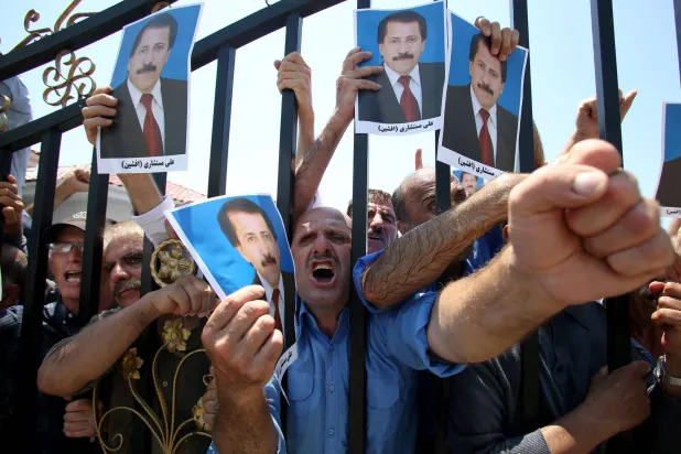 عناصر من منظمة مجاهدي خلق الإيرانية يحملون صورة شخص توفي في مداهمة الشرطة الألبانية لمخيم «أشرف 3» شمال غربي تيرانا (أ.ف.ب)