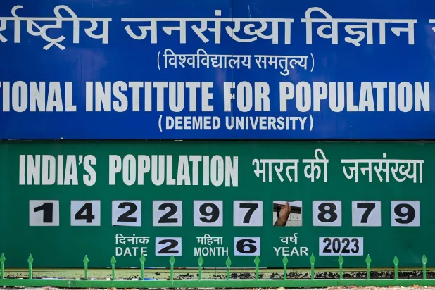 رجل أمن (تظهر يده) يغيّر يدوياً رقماً لتحديث لوحة ساعة السكان المعروضة خارج المعهد الدولي لعلوم السكان في مومباي بالهند 2 يونيو 2023 (أ.ف.ب)