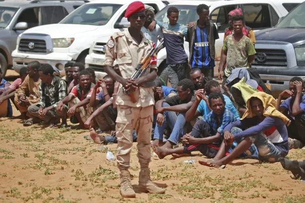 Hızlı Destek Kuvvetleri’nden bir asker, Libya’ya geçmeye çalışırken yakalanan Afrikalıların önünde (AFP)