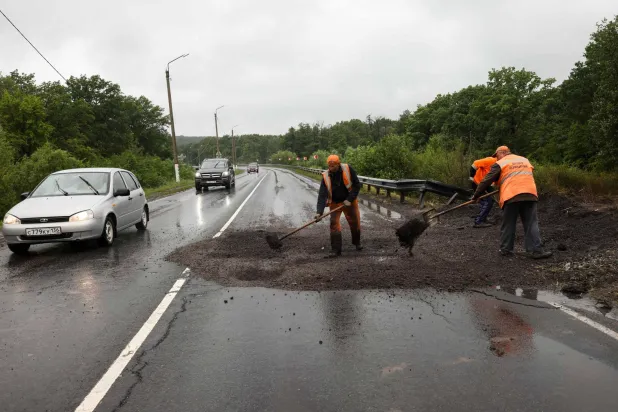 عمال يصلحون طريقًا تضرر أثناء تمرد مرتزقة فاغنر خارج مستوطنة آنا في منطقة فورونيج (أ.ف.ب)
