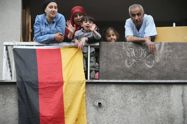 أسرة عربية تنظر من شرفتها خلال زيارة وزير الداخلية الألماني لمنطقة سولدينر كيتز التي يسكنها المهاجرون (غيتي)