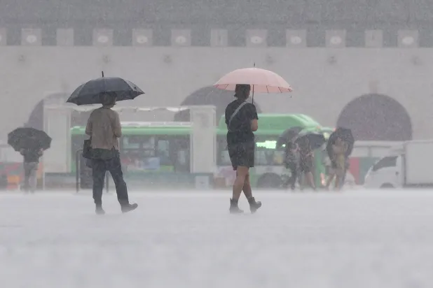 أشخاص يسيرون وسط الأمطار الغزيرة في سيول (إ.ب.أ)