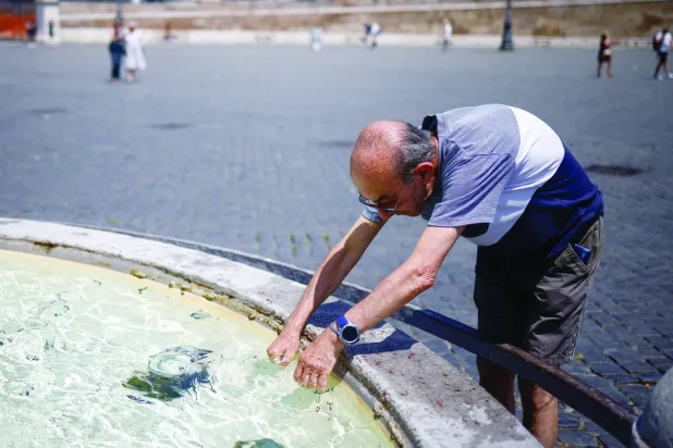 إيطالي يستريح عند نافورة في ساحة ديل بوبولو خلال موجة حارة عبر إيطاليا الجمعة (رويترز)