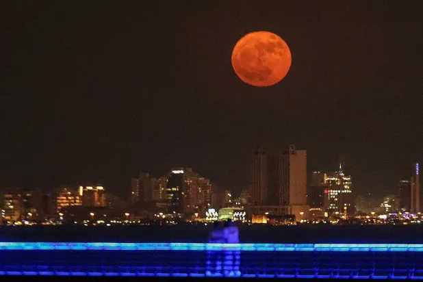 People watch as the "buck moon" rises over the skyline of Kuwait City on July 3, 2023. (AFP)