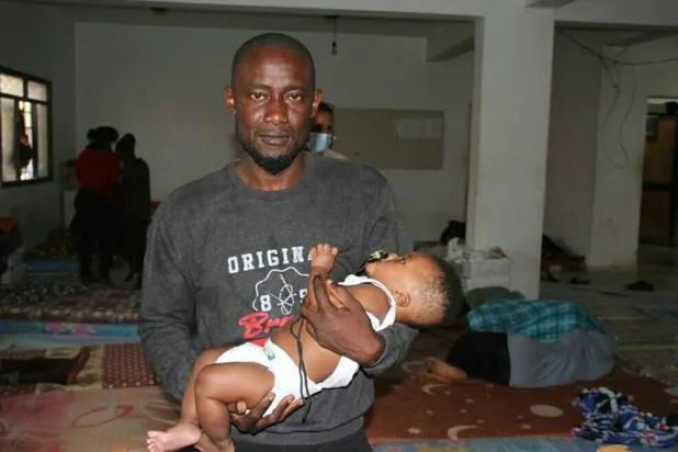 Trablus yetkilileri tarafından, başkalarıyla birlikte kurtarılan ve kucağında bebeğini tutan düzensiz bir göçmen (Ulusal Birlik Hükümeti İçişleri Bakanlığı)