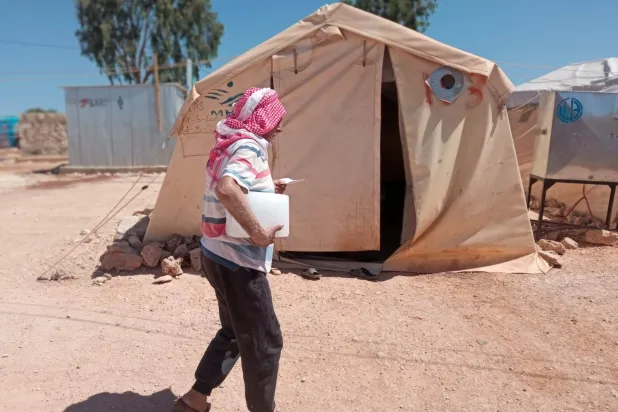 نازح سوري يحمل قطعة ثلج متجهاً إلى خيمته في مخيم «الرصيف» شمال إدلب (الشرق الأوسط)