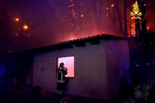 رجل إطفاء يتفحص مبنى خلال احتراق الغابات بالقرب من قرية كوركوراتشي الصقلية بالقرب من ميسينا (رويترز)